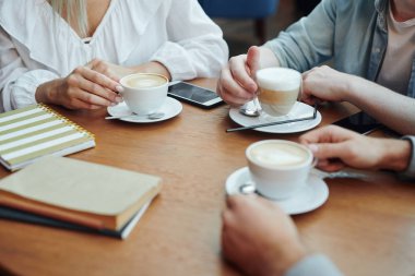 Hands of college friends gathered by table in cafe after classes, having cappuccino and consulting about homework
