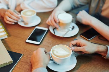 Hands of friends gathered by wooden table in cafe and having cappuccino while spending time together
