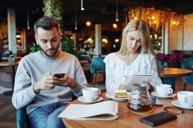 Kız arkadaşı üniversite kafesinde çay fincanı ile not defterine notlar yazarken ciddi bir adam akıllı telefondan kayıyor.