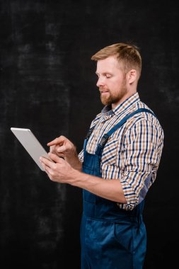 İş kıyafetlerindeki genç başarılı sakallı teknisyen izole bir şekilde kameranın önündeki dokunmatik ekranı işaret ediyor.