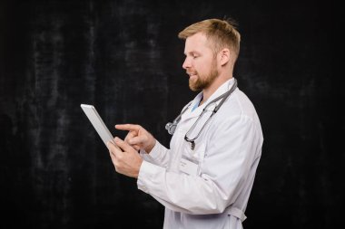 Whitecoat 'taki mutlu genç sakallı doktor dokunmatik pede kayıyor ya da izolasyonda çalışırken ekranı işaret ediyor.