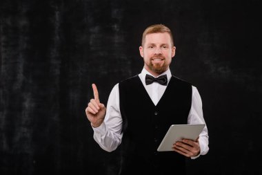 Genç ve zarif garson, dokunmatik pedi kameranın önünde, siyah arkaplanı işaret ediyor.