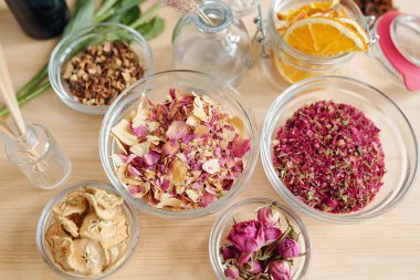 Kuru gül yaprakları, gül tomurcukları, armut ve portakal dilimleri olan cam kaseler ahşap masa üzerinde sabun yapımına hazırlanıyor.