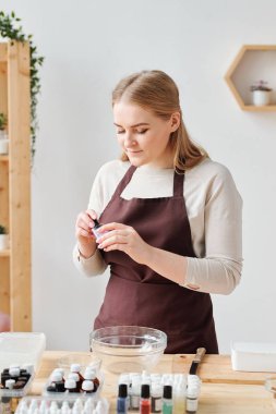 İş kıyafetli güzel bir kadın, sabun yapımında cam eşyalar arasına renk katmak için küçük bir şişe açıyor.