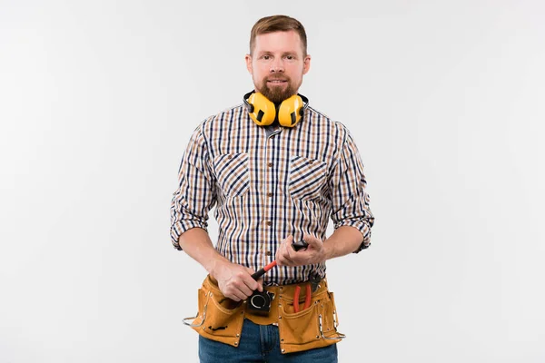 Happy Young Bearded Repairman Protective Earphones Hammer Tool Belt Standing — 스톡 사진