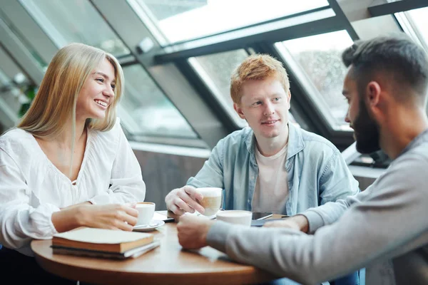 クラスの後 カフェでテーブルに座ってコーヒーを飲みながら 週の計画を話し合う幸せなカジュアルな大学生の友人のグループ — ストック写真