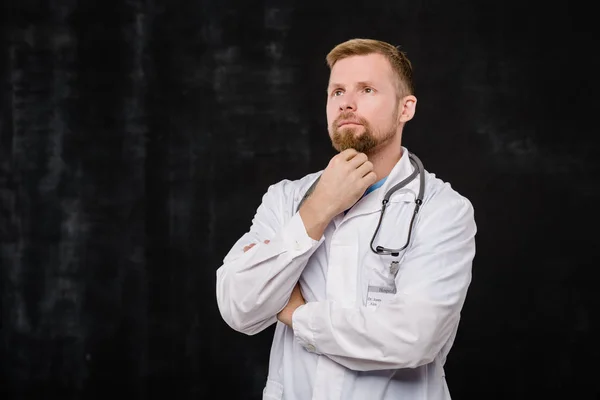 Young Bearded Clinician Pensive Expression Standing Isolation Black Background — Stock Photo, Image