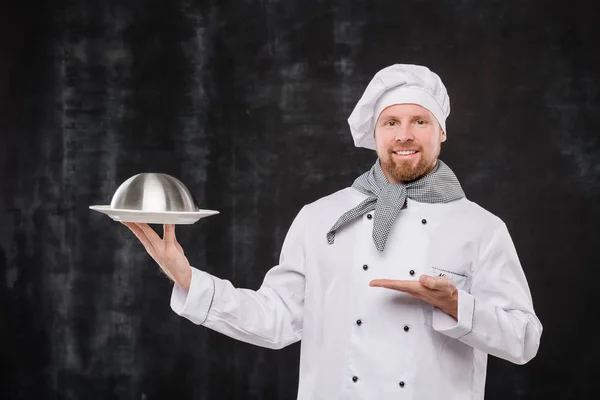 Glücklicher Bärtiger Restaurantchef Weißer Uniform Zeigt Auf Cloche Mit Gekochtem — Stockfoto