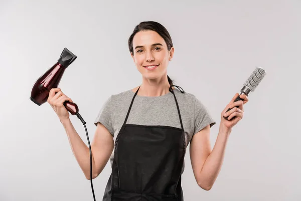 Glückliche Junge Brünette Friseurin Schürze Mit Haartrockner Und Haarbürste Während — Stockfoto