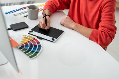 Grafik tableti ekranı üzerinde stili olan genç serbest tasarımcının elleri masadaki fotoğrafları rötuşluyor