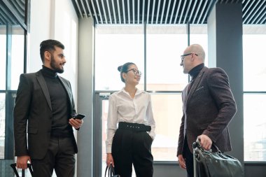 Young Asian businesswoman consulting with her mature colleague with elegant businessman standing near by