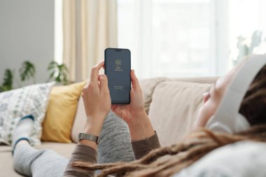 Kanepede uzanmış dinleyecek bir şey ararken akıllı telefonu elinde tutan genç bir kadının elleri.