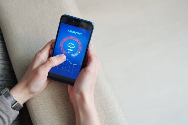 Akıllı telefonlu genç bir kadının elleri dokunmatik ekranda grafik ve diyagramla hava raporuna bakıyor.