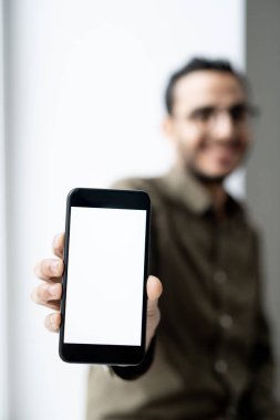 Kameranın önünde duran genç ve çağdaş iş adamının elinde boş ekranlı akıllı telefon.