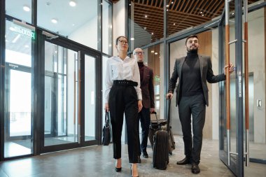 Group of intercultural business travelers with baggage entering hotel lounge to order rooms for living