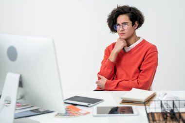 Genç yaratıcı web tasarımcısı bilgisayar ekranının önünde otururken yeni çevrimiçi proje üzerinde çalışmaya odaklanıyor