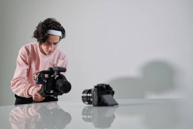 Genç ciddi video blogcusu stüdyoda çekim yaparken yeni fotoğraf ekipmanlarının önünde duruyor.