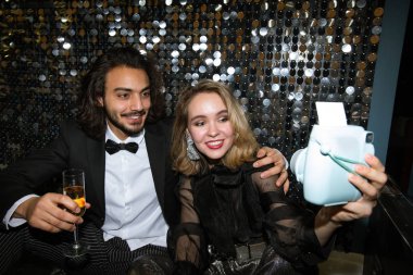 Göz kamaştırıcı giysiler içinde genç ve mutlu bir çift fotoğraf makinesinde parıldayan bir duvarla kendilerini çekiyorlar.