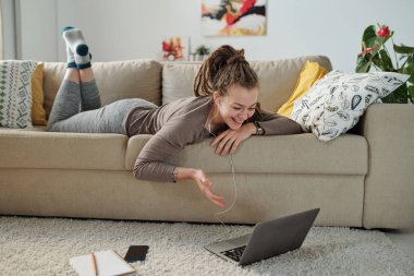 Kulaklıklı neşeli kız evde görüntülü sohbet yoluyla arkadaşınla konuşurken dizüstü bilgisayara bakıyor.