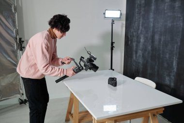 Genç çağdaş video blogcusu kamerasıyla stüdyoda yeni fotoğraf ekipmanları çekiyor.