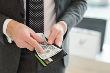 Takım elbiseli, zengin, genç ve zarif iş adamının elleri cüzdan ve dolar banknotları tutuyor.