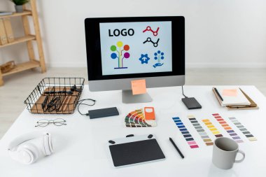 Ekranda logosu olan bilgisayar monitörü, masasında stilus, kupa, palet ve diğer şeylerle birlikte grafik tableti