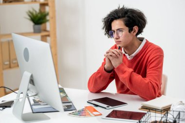 Yeni web sitesi üzerinde çalışırken bilgisayar ekranına bakan çenesinde kalemle ciddi bir yaratıcı tasarımcı.