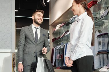 Güzel tezgahtar sayesinde genç ve neşeli işadamı, elinde kağıt torbalarla alışveriş yapıyor.