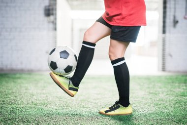 Genç bayan futbolcunun ayaklarının üzerinde duran futbol topuyla antrenman sırasında yeşil sahada duran alt kısmı.