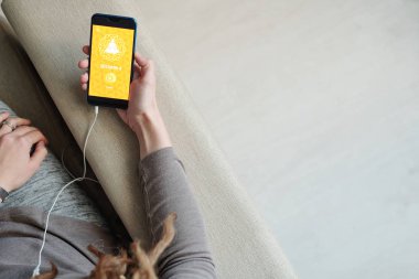 Akıllı telefonlu genç bir kadının kanepede oturup yoga kursunun videosunu izlemesinin özeti.