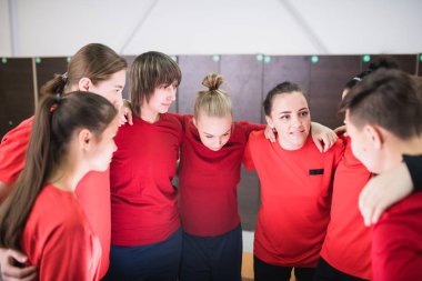 Kırmızı tişörtlü geniş bir grup genç sporcu, çember oluşturup yaklaşan oyunu kucaklıyor ve tartışıyorlar.