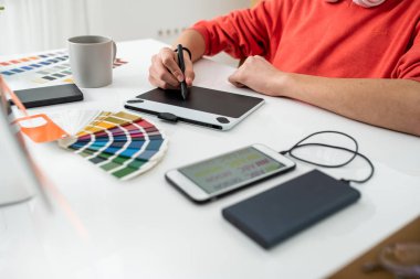 Genç serbest çalışan web tasarımcısının elleri resim tableti ekranı üzerinde stilus tutarken masadaki resimlere rötuş yapıyor