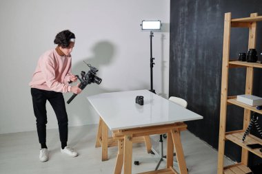 Genç video blogcusu stüdyoda masa başında dururken yeni fotoğraf ekipmanları çekiyor.