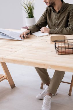 Genç iş adamı ya da öğrenci dergideki makaleye bakıyor ve ödevlerini hazırlarken notlar alıyor.