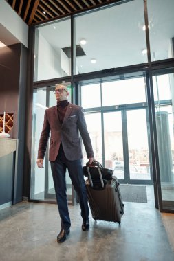 Mature male business traveler pulling suitcase while entering hotel lounge after arrival in foreign country