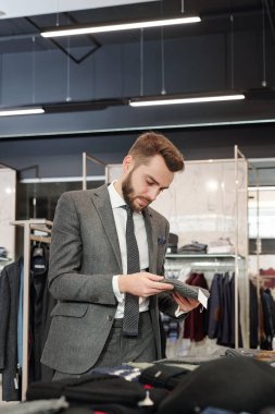 Çağdaş butikte yeni koleksiyon arayan ve yeni örülmüş bereyi seçen iyi giyimli genç bir adam.