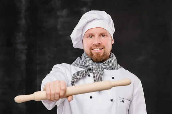 快乐的大胡子厨师 身穿制服 在镜头前拿着木制滚针头看着你 — 图库照片