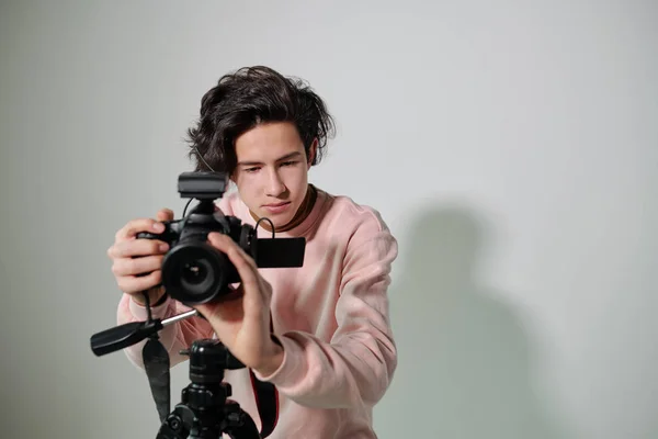 年轻摄影师穿着粉红运动衫站在白墙边 在拍摄前调整录像设备 — 图库照片