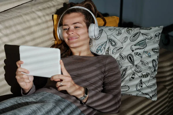 幸せな若いです若いです女性リラックスしていますソファに見ながら面白いですビデオでTouchpadで暗い部屋 — ストック写真