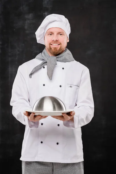 Νεαρός Χαμογελαστός Σεφ Στολή Κρατώντας Πανιά Μαγειρεμένο Γεύμα Για Εσάς — Φωτογραφία Αρχείου