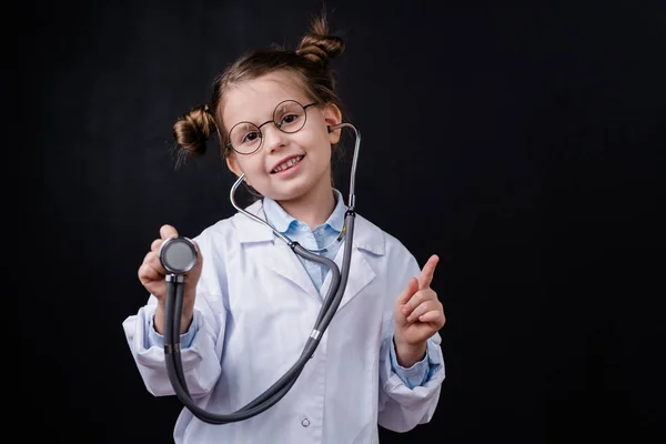 Χαρούμενο Κοριτσάκι Λευκό Παλτό Που Χρησιμοποιεί Στηθοσκόπιο Ενώ Δείχνει Μπροστά — Φωτογραφία Αρχείου
