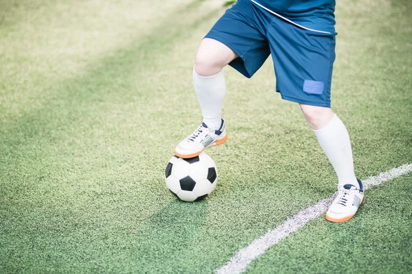 Mavi üniformalı genç aktif bayan oyuncunun bacakları sahada futbol oynarken sağ ayağını topun üzerinde tutuyor.