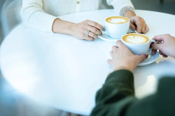 休憩中にカプチーノを飲みながらカフェに座っている2人の若いフレンドリーな女性の手 — ストック写真