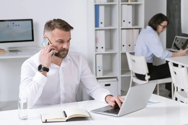 Akıllı Telefonlu Ciddi Bir Adamı Ortağıyla Konuşurken Bilgisayardaki Bilgilere Bakıyor — Stok fotoğraf