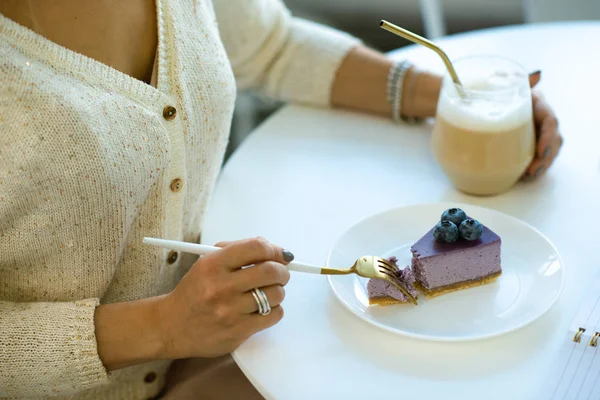 カプチーノを飲みながらおいしいブルーベリーチーズケーキを食べながらカフェのテーブル席に座る若い女性の手 — ストック写真