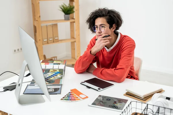 自宅で新しいロゴの上で作業しながら コンピュータ画面を見て眼鏡の若い普及したウェブデザイナー — ストック写真