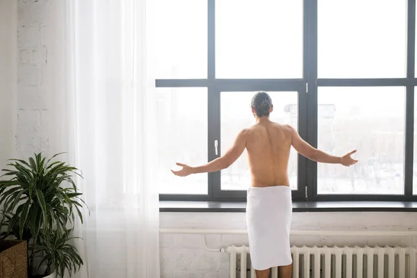 年轻男子洗澡后伸出手透过窗户时 腰部裹着白毛巾的后视镜 — 图库照片