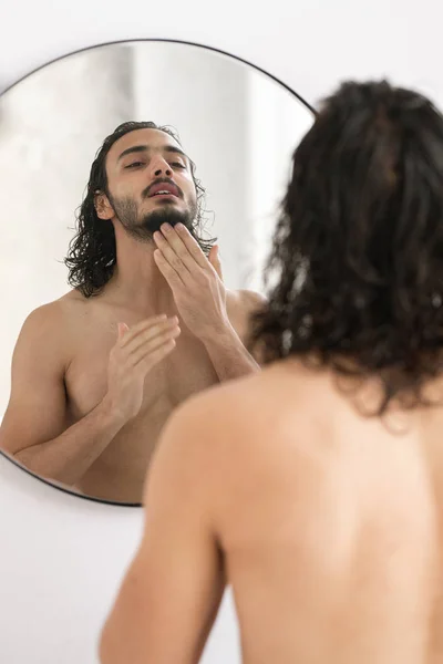 早上洗完澡后 赤裸裸的年轻人一边去刮胡子 一边照着镜子里的胡子 — 图库照片