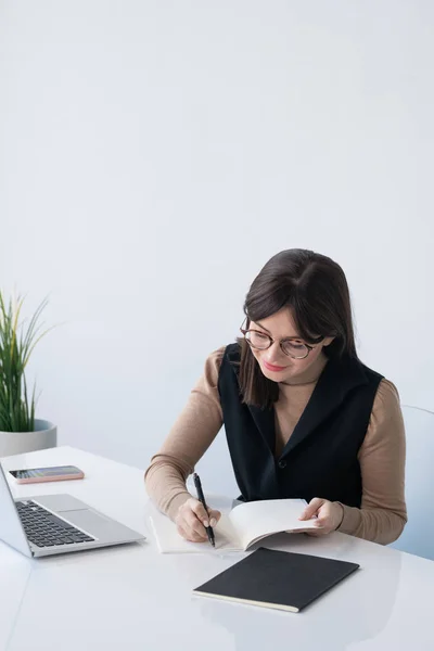 若い成功した実業家ノートパソコンの前で机の前に座って仕事の日の計画を書き留める — ストック写真
