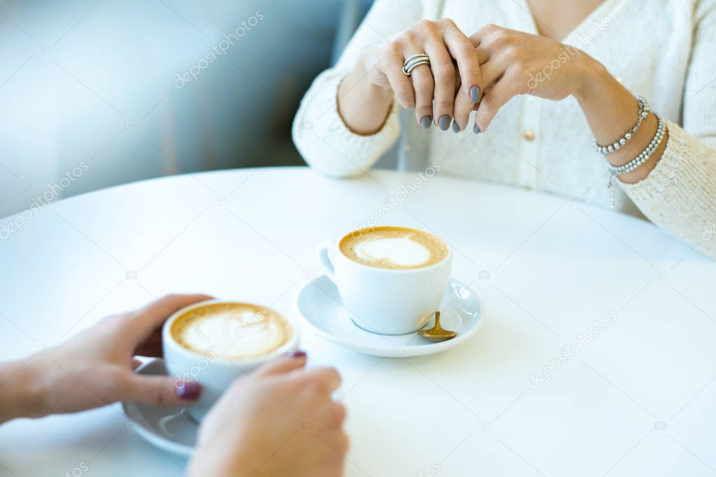 Hands of two young friendly women in casualwear sitting by table in cafe while having cappuccino during conversation at break